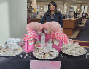 A person behind a table full of fashion accessories and pink gift bags