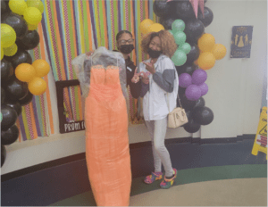 Two people standing near a mannequin with an orange dress